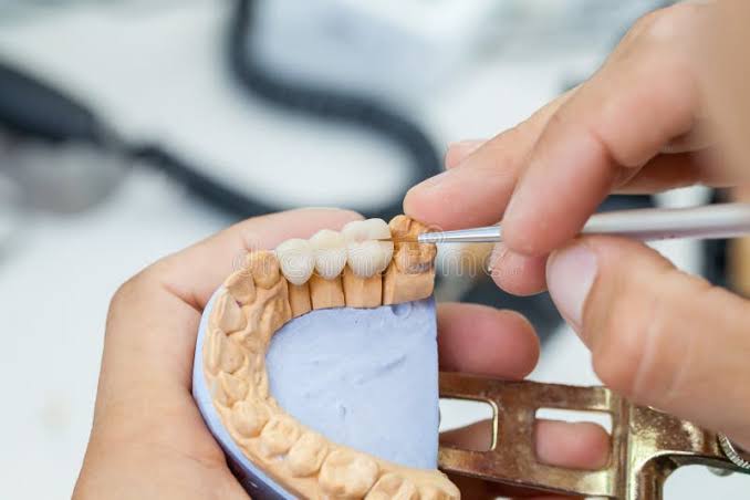Dental ceramicist in white coat meticulously layering porcelain powder under a precision light source